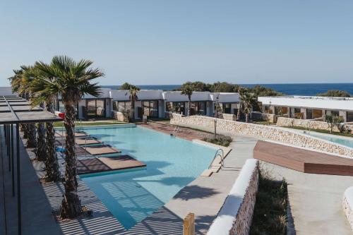 a swimming pool with palm trees and a building at Barceló Nura in Sant Lluis