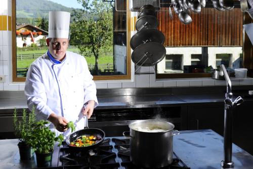 a chef in a kitchen preparing food in a pan at Hotel Serles in Mieders