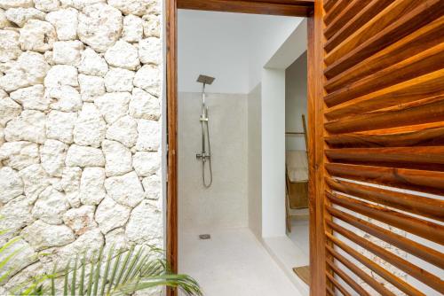 a bathroom with a walk in shower next to a stone wall at Coconut Villas Zanzibar in Matemwe