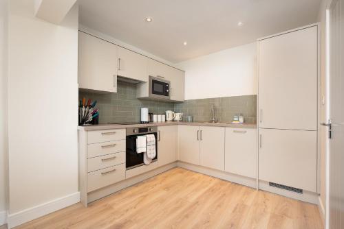 a kitchen with white cabinets and a wooden floor at Unique 2Bedroom Flats in Bicester in Bicester