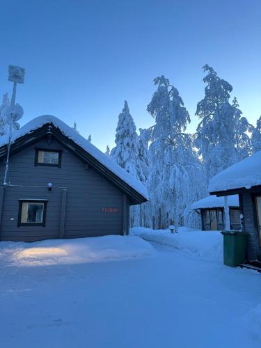 a house covered in snow with trees in the background at Pusikko - Cozy Lake Villa - Ice Swimming - Sauna - Fireplace - Barbeque Shed in Kuusamo
