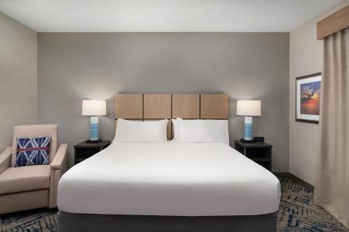 a bedroom with a large white bed and a chair at Candlewood Suites Gonzales - Baton Rouge Area by IHG in Gonzales