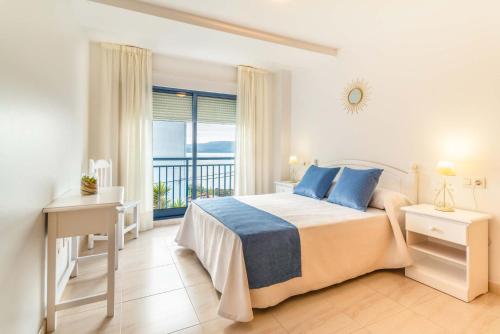 a white bedroom with a bed and a balcony at Apartamentos Punta Lucero en Portonovo in Portonovo