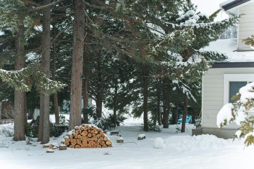 a pile of logs in the snow next to a house at Ubaku Villa 宇莫別荘 in Biei