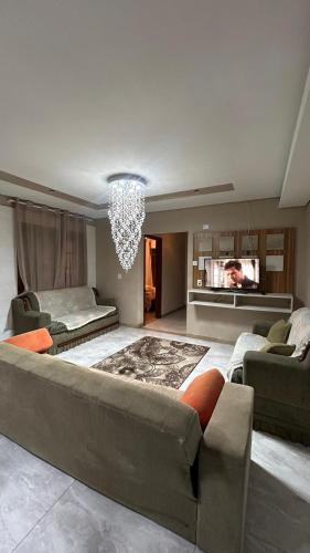 a living room with a large couch and a chandelier at Suíte por do sol 2 casa compartilhada in Xangri-lá
