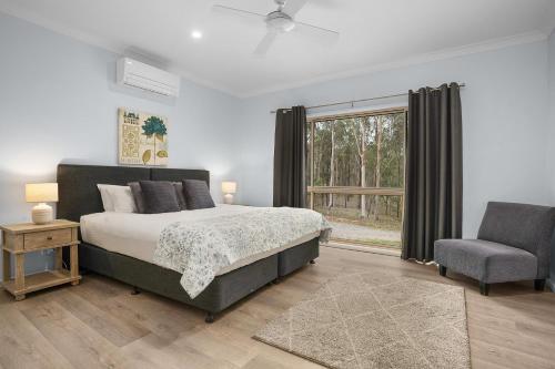 a bedroom with a bed and a chair and a window at 27 Rows on Hermitage in Pokolbin