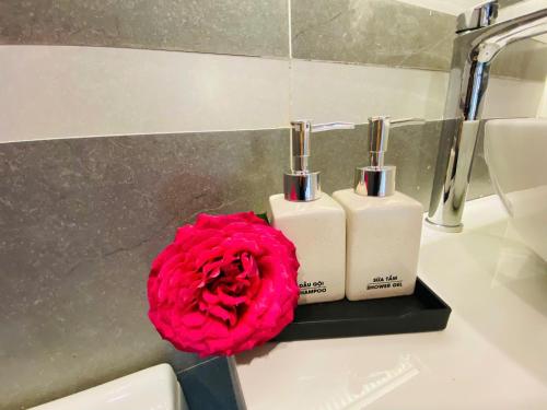 a red rose next to two soap bottles on a bathroom sink at Peace Homestay Hoa Lư in Xuân Sơn