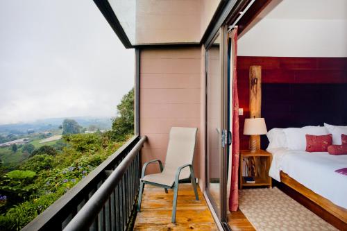 a bedroom with a bed and a chair on a balcony at Poas Volcano Lodge in Vara Blanca
