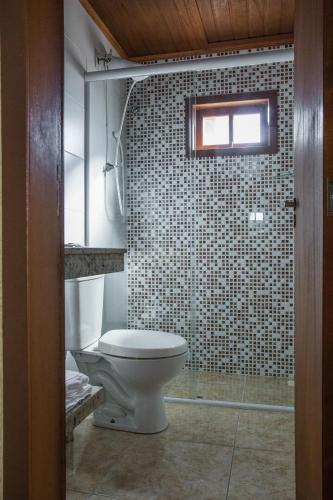 a bathroom with a toilet and a tile wall at Pousada Areias do Rosa in Praia do Rosa