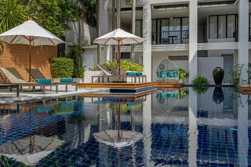 a swimming pool with two umbrellas in front of a building at OUTRIGGER Surin Beach Resort in Surin Beach
