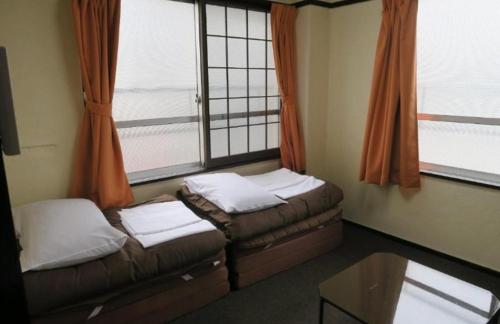 a room with two beds and a table and windows at 高松guesthouseOLD in Takamatsu