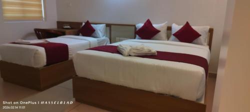 two beds in a hotel room with red pillows at Hotel Eden Palace in Trichūr