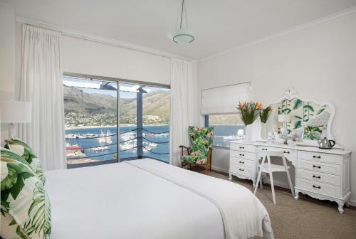 a bedroom with a bed and a desk and a window at Poseidon Guest House in Hout Bay