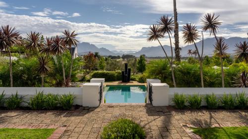a swimming pool in a garden with palm trees and mountains at Wild Mushroom Country House in Stellenbosch