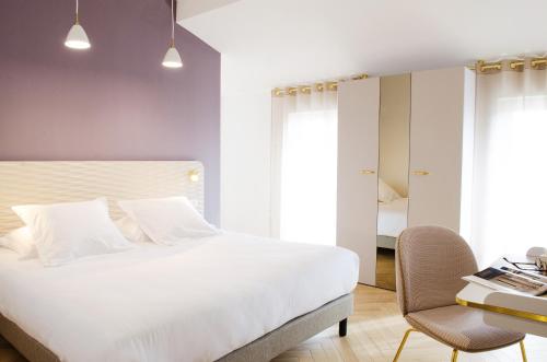 a bedroom with a large white bed and a chair at Hôtel le XIX in Béziers