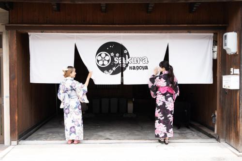 two women in kimonos standing in front of a banner at sakura.nagoya in Nagoya