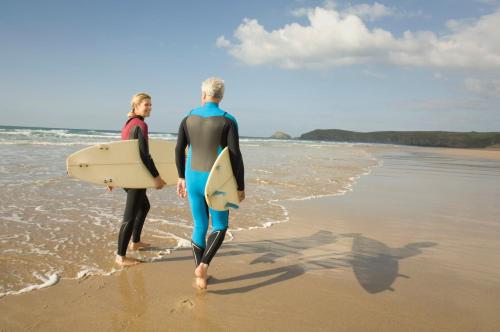 two men walking on the beach with their surfboards at Penryn Quayside Apartment – 1-bed, Fully Equipped Waterside base in Penryn