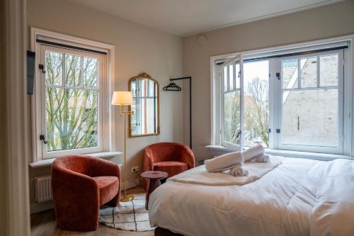 a bedroom with two chairs and a bed and two windows at Hotel By Atelier in Nijmegen
