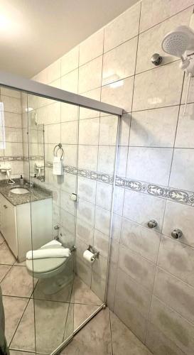 a bathroom with a toilet and a glass shower stall at Pousada Cores De Outono in Canela