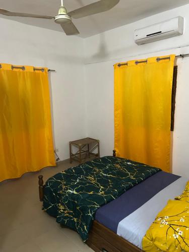 una camera da letto con tende gialle e un letto di Maison blanche a Cotonou