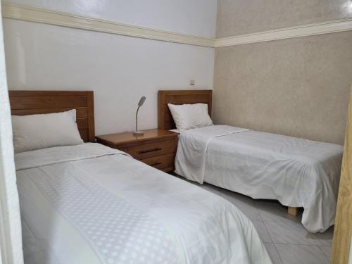 a bedroom with two beds with white sheets and a lamp at Appartement Imi-Ouaddar 2 in Agadir nʼ Aït Sa