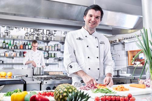 a chef preparing food in a kitchen with other chefs in the background at Hotel Tannenmühle in Grafenhausen