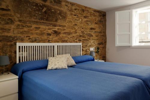 a bedroom with a blue bed with a stone wall at Pensión Rua Nova in Santiago de Compostela