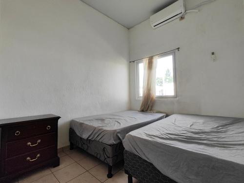 two beds in a room with a window and a dresser at La casa de Alex in San Juan Opico