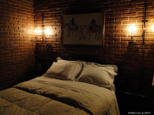 a bed with two lights on a brick wall at Pousada Romântica Serra da Mata in Penedo