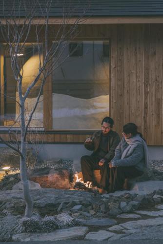 two people sitting by a fire in front of a building at Peanuts Nest in Nagano