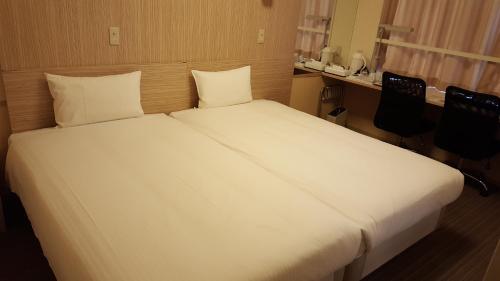 a large white bed in a room with two chairs at Smile Hotel Shirakawa in Nishigo