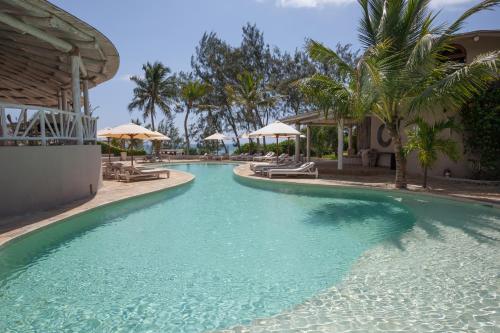 a pool at a resort with blue water and palm trees at Kobe Suite Resort in Watamu
