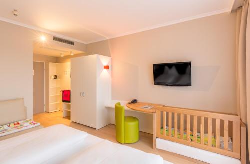 ein Schlafzimmer mit einem Kinderbett und einem TV an der Wand in der Unterkunft All in Red Thermenhotel in Lutzmannsburg