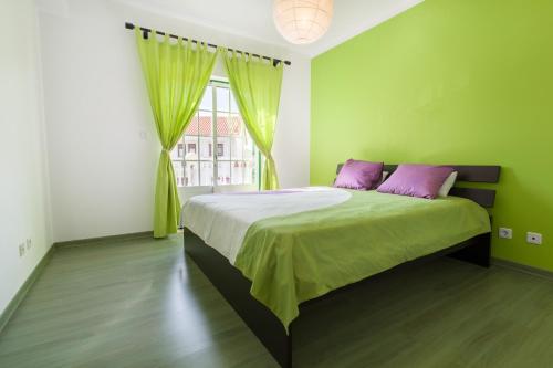 um quarto verde com uma cama grande e almofadas roxas em Casa Bordalo - Family, Beach, Culture and Surf nas Caldas da Rainha