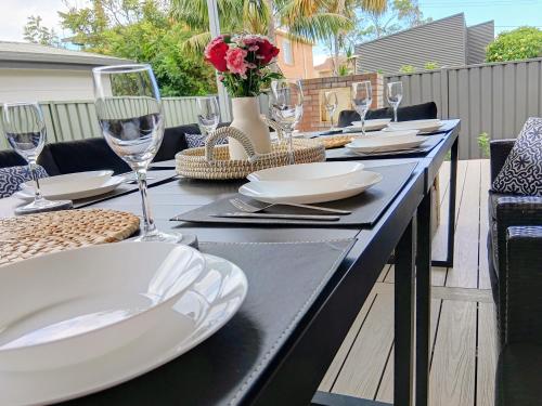 a table with plates and wine glasses on a patio at 100m to Beach&Shop Spacious Pristine One Story Family Home in Batemans Bay
