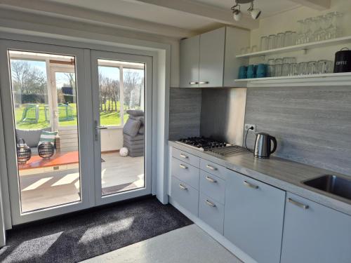 a kitchen with white cabinets and a sliding glass door at Vrijstaande ruime familiewoning landelijk gelegen in Lewedorp