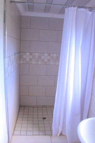 a shower with a white shower curtain in a bathroom at Exodus Guesthouse Mahlakwena Stee'lpoort in Steelpoort