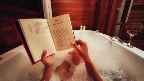 a person sitting in a bath tub reading a book at Chale Allegra - Hidro Aquecida - Vista para o Lago in Venda Nova do Imigrante