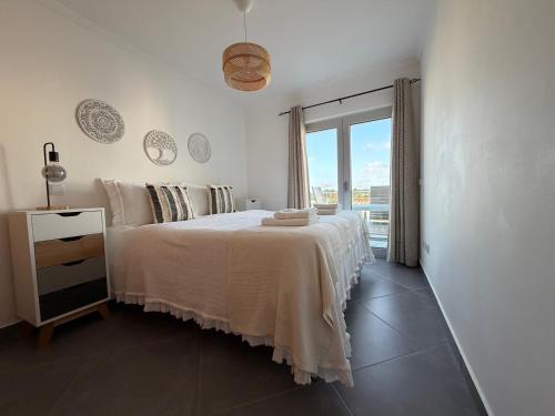 a white bedroom with a bed and a window at Vela Terrace in Monte Gordo