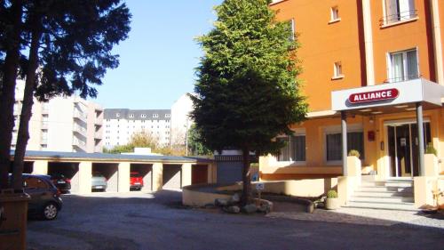 uma árvore num parque de estacionamento em frente a um edifício em Hôtel Alliance em Lourdes