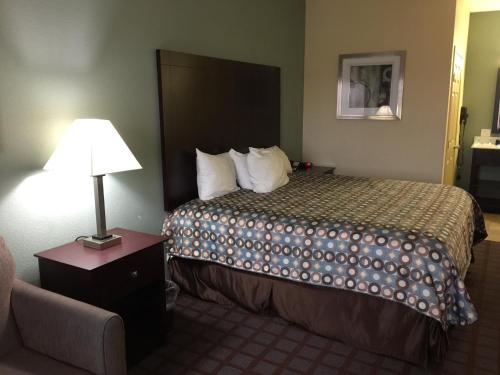 a hotel room with a bed with a lamp and a chair at Pearsall Inn and Suites in Pearsall