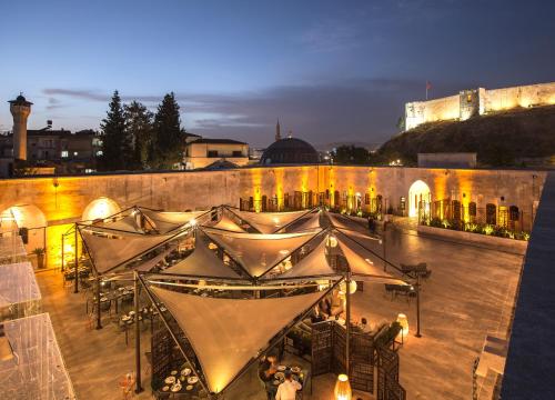 een groep mensen die aan tafels voor een gebouw zitten bij HSVHN Hotel Hışvahan in Gaziantep