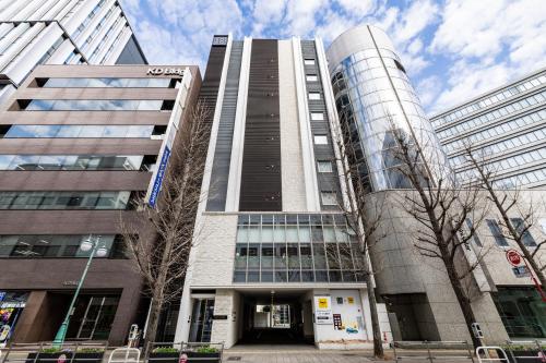 a tall building in a city with trees in front of it at KOKO HOTEL Hakata Shinkansenguchi - formerly Hotel Wing International Hakata Shinkansenguchi in Fukuoka