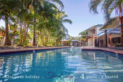 a swimming pool with palm trees next to a building at Edge on Beaches Agnes Waters 1770 in Agnes Water