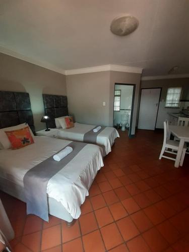 two beds in a hotel room with a table and chairs at Oakwood Lodge in Bloemfontein