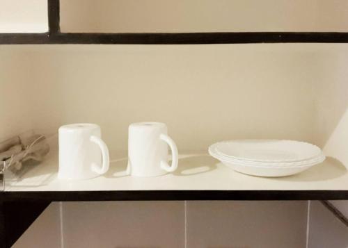 two white mugs and a plate on a shelf at Cozy Studio Condo with Stunning Tagaytay Views in Tagaytay