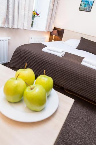 four green apples on a plate on a table next to a bed at Ivolita Vilnius in Vilnius