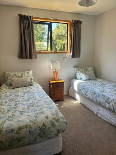 a bedroom with two beds and a lamp and a window at Flax Ridge in Hokitika Airport
