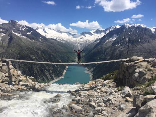 a man standing on a suspension bridge over a mountain lake at Hotel Garni Elisabeth in Zell am Ziller