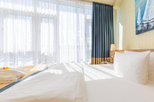 a bedroom with a white bed with a large window at Strand-Hotel Hübner in Warnemünde